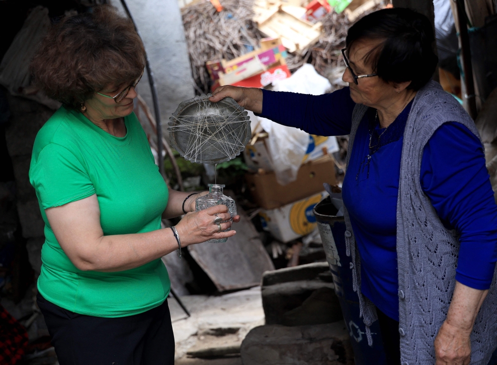 Ariana Nikolla (L) and Resmie Tuci prepare rose water in the traditional way in Permet, some 250km Southwest of the capital Tirana, on May 28, 2025.  In Permet, deep in the spectacular Vjosa Valley of southern Albania, roses rule supreme, whether used to make perfumes, flavoured water or the Turkish delight sought out by thousands of sweet-toothed tourists.  (Photo by Adnan Beci / AFP)

