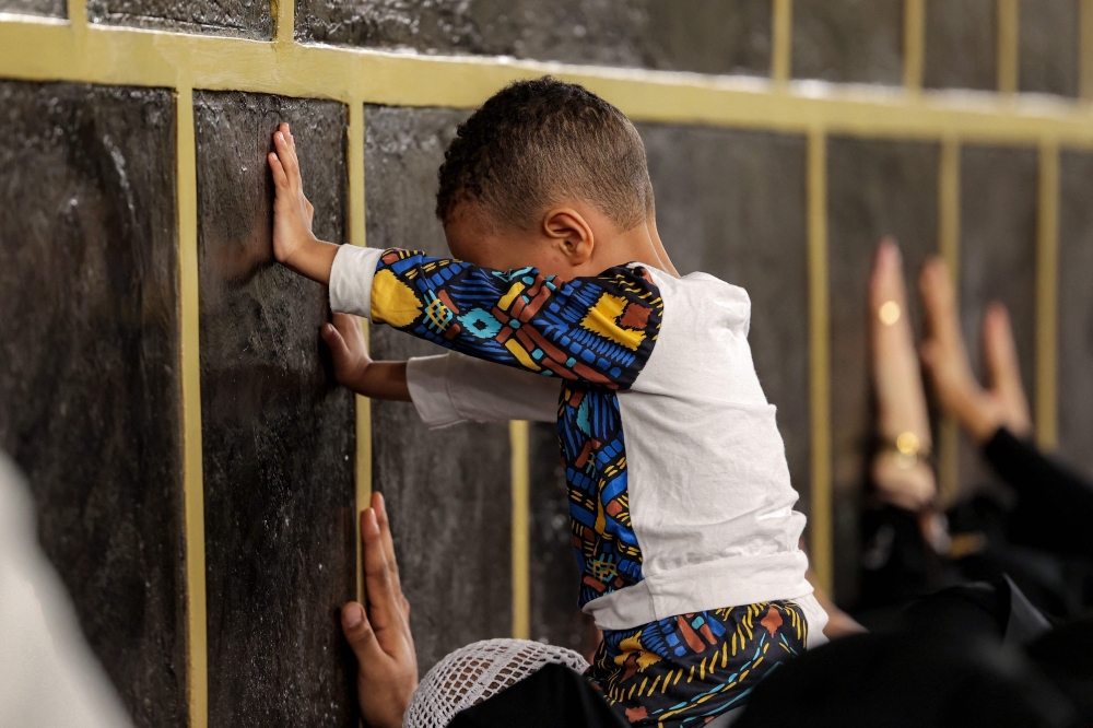 A young boy is lifted up to touch the Kaaba, in the holy city of Mecca. — AFP