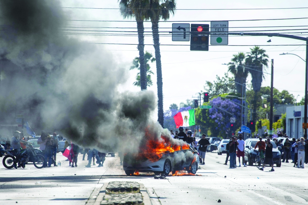 A car burns as a demonstrator waves a Mexican national flag during a protest, in the Compton neighbourhood of Los Angeles. — AFP