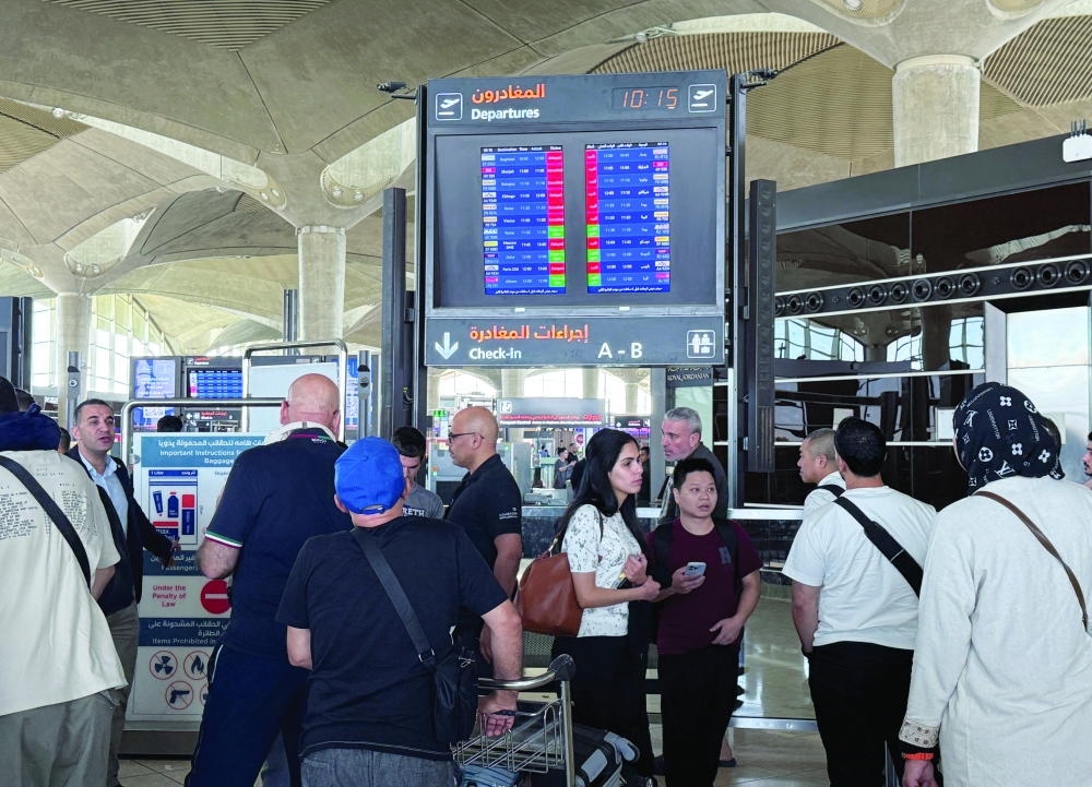 People stand in front of a flight information display screen showing information about delayed and cancelled flights, at Queen Alia International Airport in Amman. — Reuters