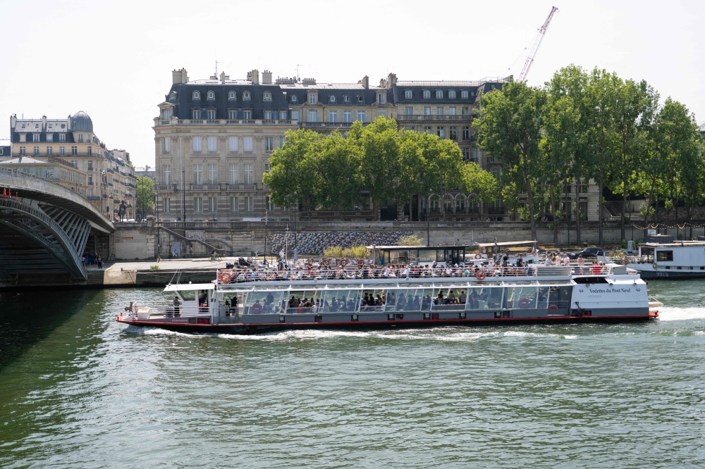 Tourists stand on a bateau mouche (tourism boat cruises) before passing under a bridge on the Seine river during a warm afternoon, in Paris, on June 13, 2025.  (Photo by Emma DA SILVA / AFP)
