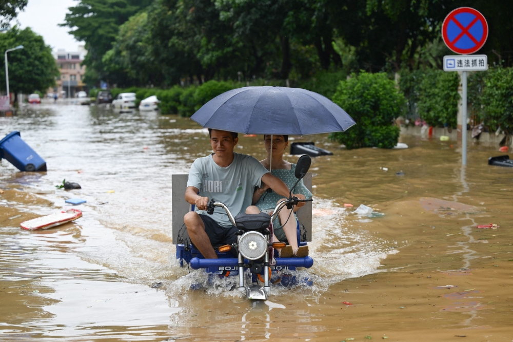 People ride a motorcycle through a flooded street in Zhongshan, China. — AFP