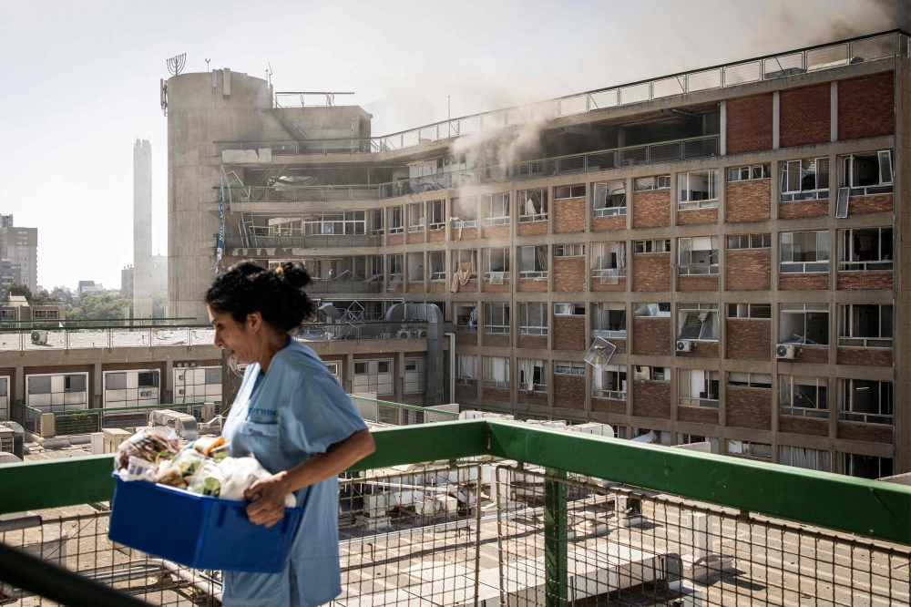 A nurse carries medical supplies past a building with smoke billowing out, in southern Israel. — AFP