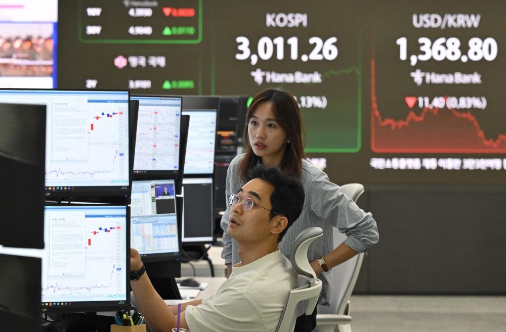 Currency dealers monitor exchange rates in front of a big screen showing South Korea's benchmark stock index (C top) and the Korean won/USD exchange rate in a foreign exchange dealing room at the Hana Bank headquarters in Seoul. — AFP