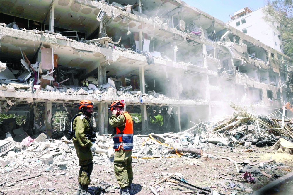 Israeli security forces look on as a digger clears the rubble of a destroyed building. — AFP 