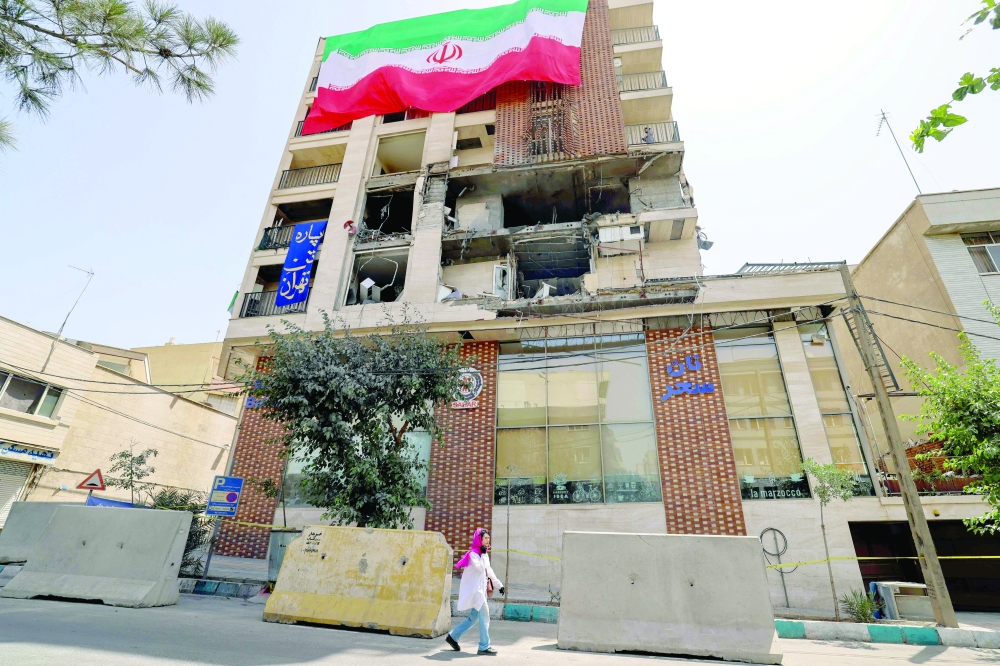 A woman walks past a residential building that was hit in an Israeli strike covered with a big Iranian flag, in Tehran on Wednesday.  — AFP