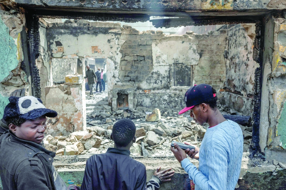 Residents look through a window to assess the damage in a commercial building that was vandalized and torched during deadly protests marking one year since the storming of parliament in anti-tax demonstrations in Nairobi. - AFP

