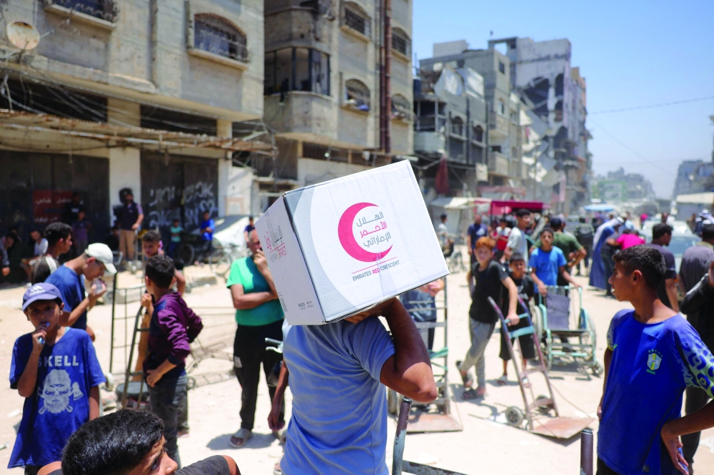 A Palestinian man carries away a food parcel donated by the Emirates Red Crescent, from a distribution point supervised by volunteers to prevent theft in Gaza City. - AFP