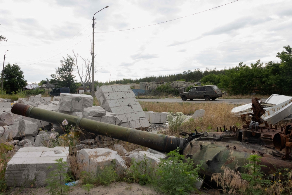 A car drives along the road past a partialy burnt tank in the city of Svyatohirs'k, Donetsk region. — AFP