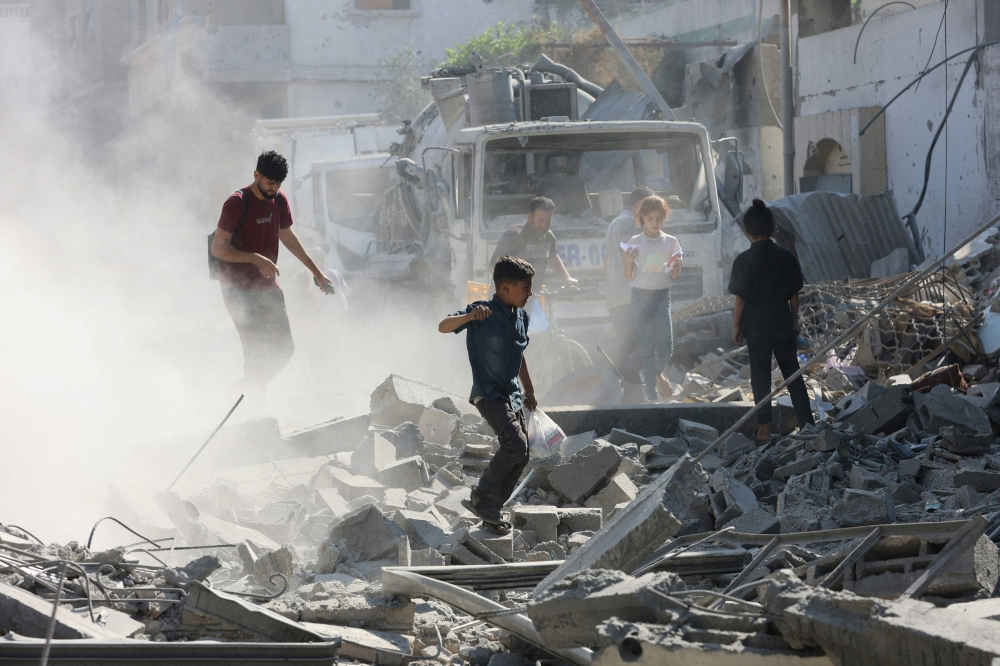 Palestinians walk through through rubble following Israeli strikes in Jabalia in the northern Gaza Strip. — AFP