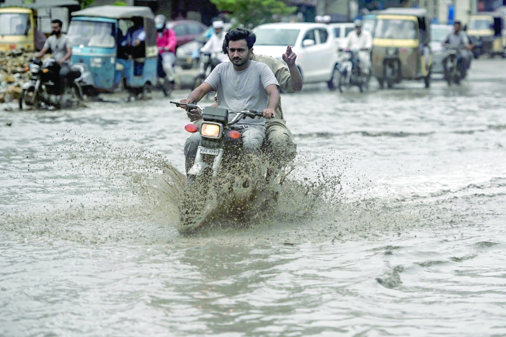 Commuters make their way through a flooded street after heavy rainfall in Karachi on June 28, 2025. 