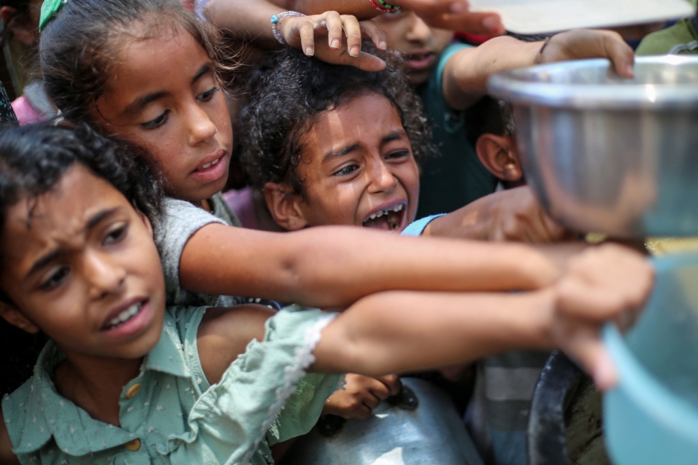 Palestinian children line up to receive a hot meal at a food distribution point in Nuseirat. - AFP