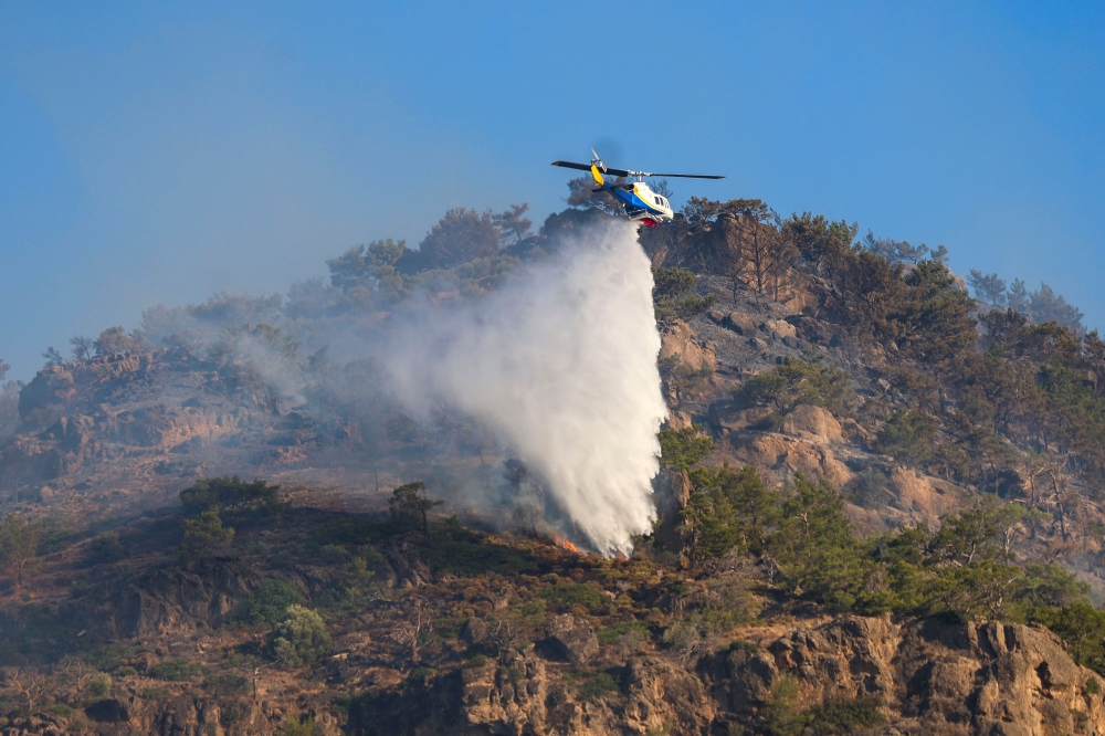 An helicopter drops water on a wildfire that broke out in Ierapetra at the southern Greek island of Crete, on July 3, 2025. A forest fire fanned by gale-force winds in the Greek holiday island of Crete led to the evacuation of locals and tourists, officials said on July 3, 2025. Greece is in the midst of a heatwave that is searing large chunks of Europe. (Photo by Costas Metaxakis / AFP)