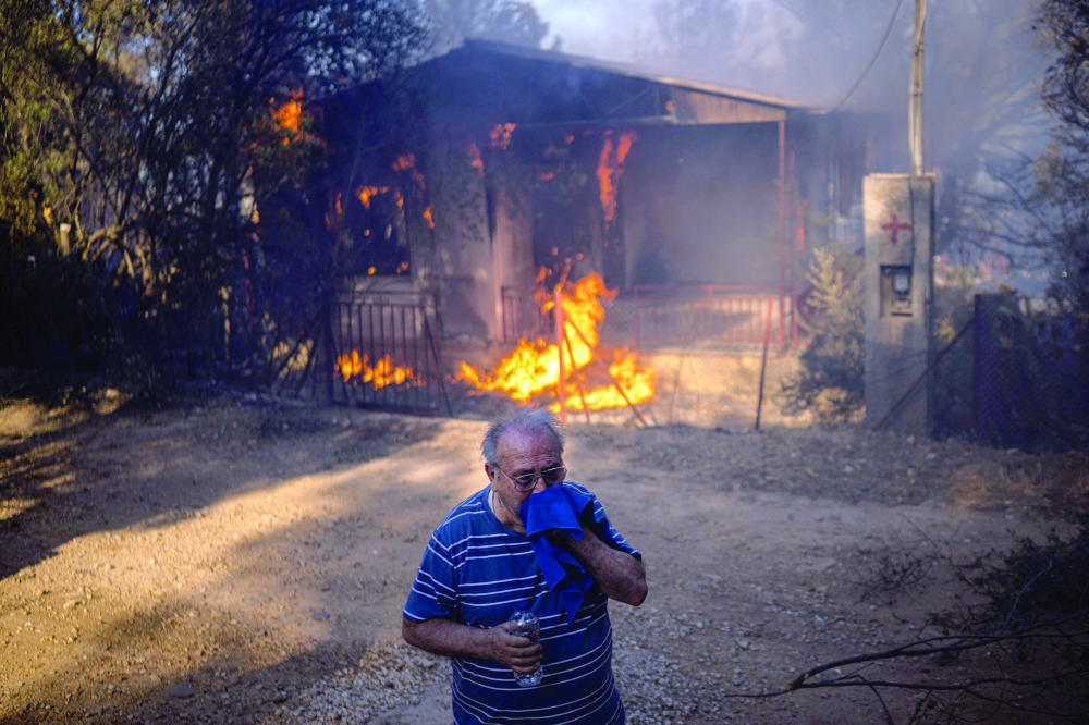 A man stands in front of a house burning during a wildfire in Pikermi, east of Athens. — AFP