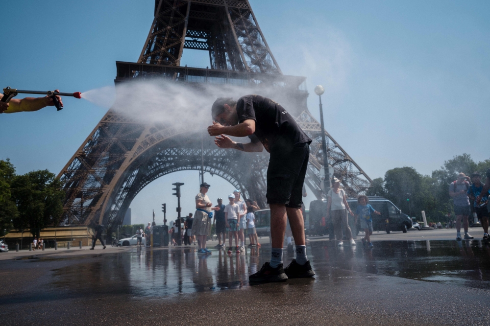 A municipal employee sprays water to cool off tourists in front of the Eiffel Tower in Paris, on July 2, 2025, as a heatwave hits France. France registered its second-warmest June since records began in 1900, said the country's ministry for ecological transition on July 2, 2025, as Europe swelters under an early summer heatwave. (Photo by Dimitar DILKOFF / AFP)

