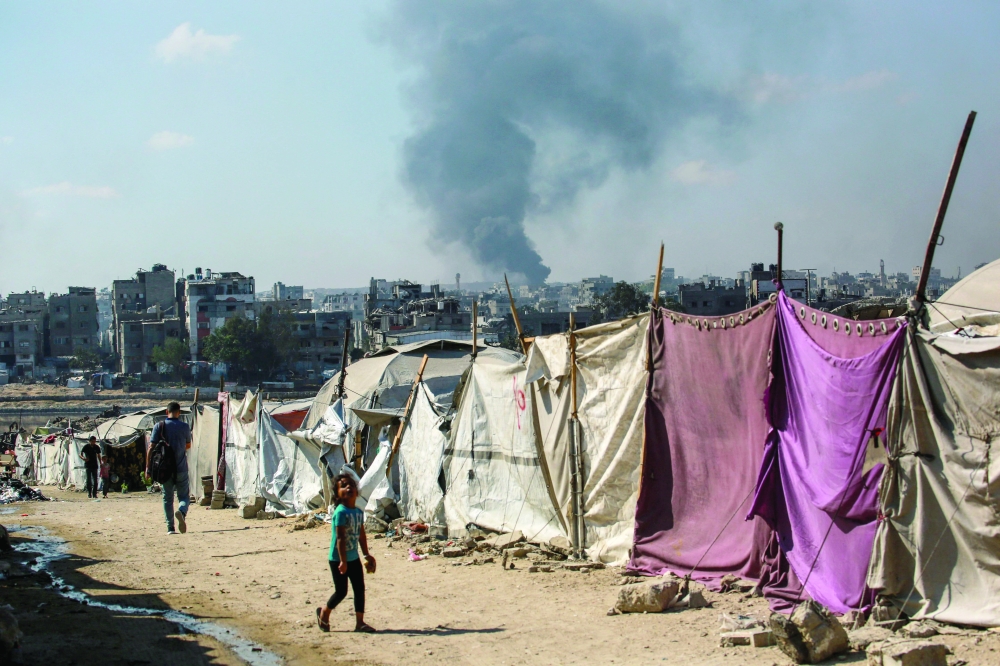 People walk past makeshift shelters as smoke billows east of Gaza City. — AFP