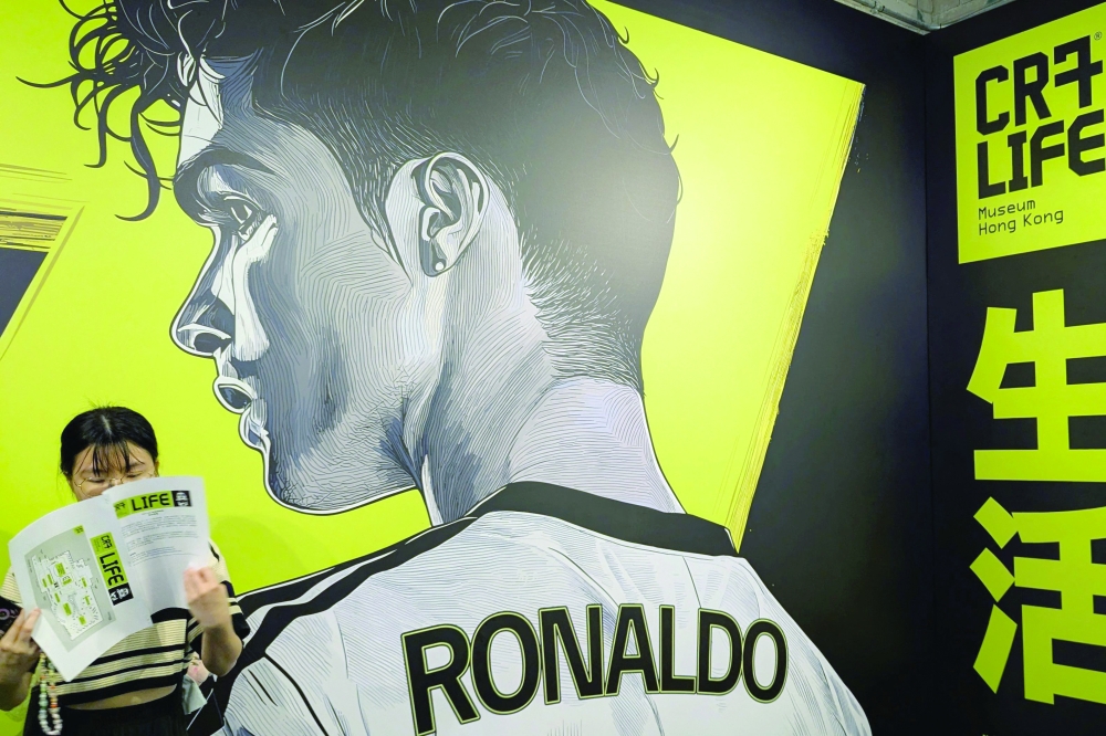 A visitor (L) stands in front of a large mural of footballer Cristiano Ronaldo during the opening of the CR7 LIFE Museum in Hong Kong on July 7, 2025. 