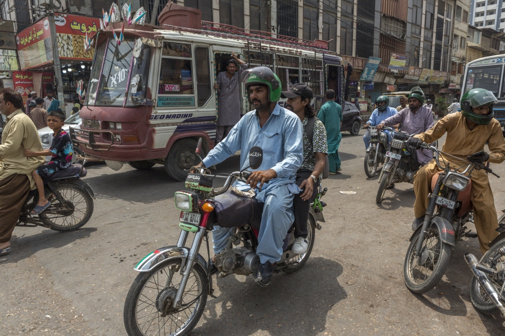 Shahbaz Ali, a ride-hailing motorcycle driver who earns $8 on a good day, transports a passenger through the busy streets of Karachi, Pakistan, June 26, 2025. (Asim Hafeez/The New York Times)