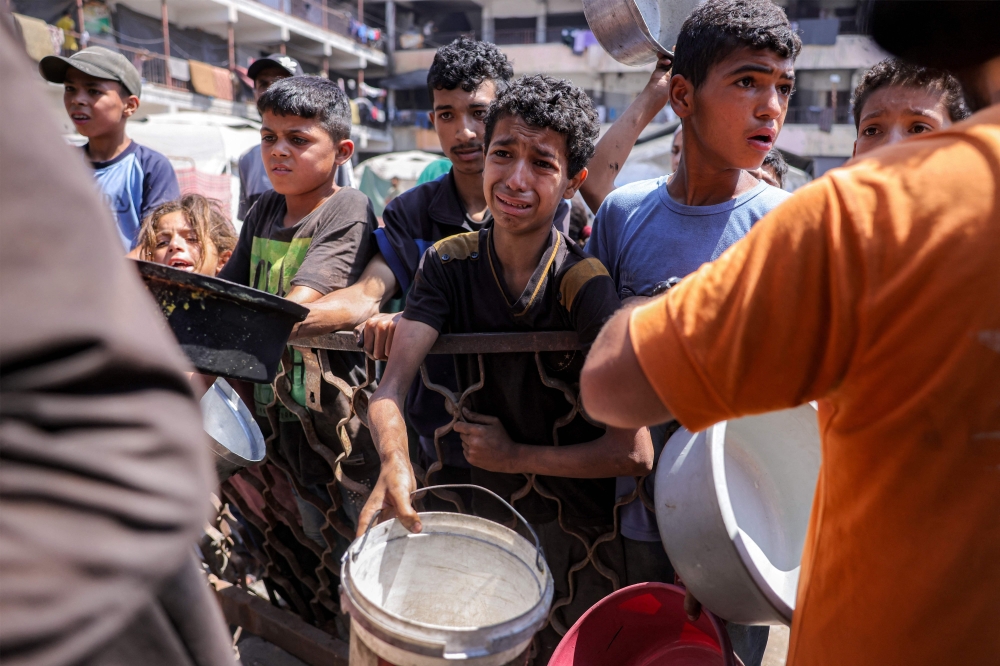 Children queue with pots to receive meals from a charity kitchen in Gaza City. — AFP