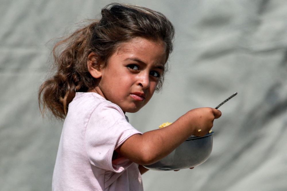A girl eats from a dish after queueing for a meal from a charity kitchen in Gaza City on Monday. — AFP  