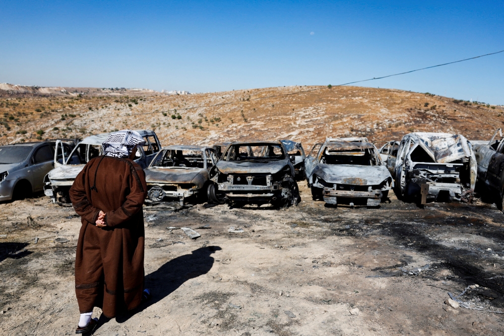 A Palestinian man inspects burnt cars, 