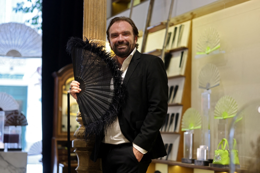 French luxury hand fan designer Olivier Bernoux poses with one of his fan creation in his store in Madrid, on July 4, 2025.  The Spanish must-have item has retained its relevance thanks to designer creativity and amid increasingly oppressive summer temperatures stoked by climate change. (Photo by Thomas COEX / AFP)

