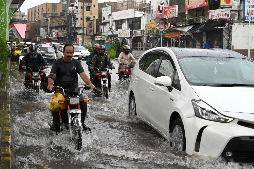 Commuters make their way through a flooded street during heavy monsoon rains in Rawalpindi. - AFP 