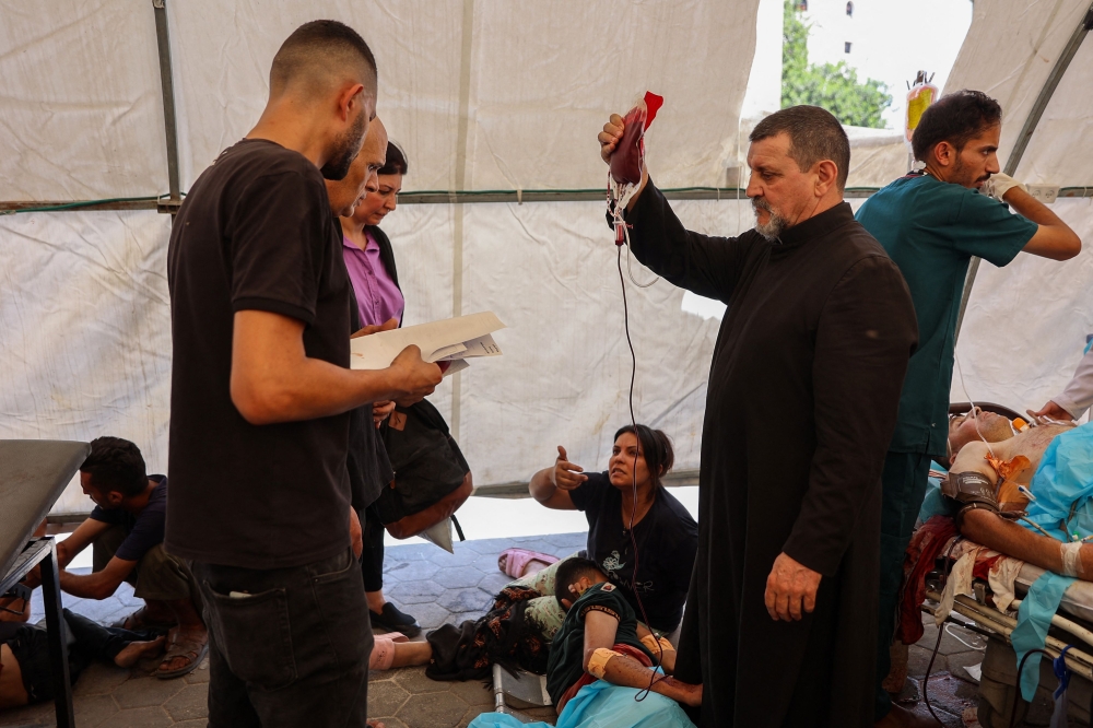 Father Carlos (C) from the Holy Family church in Gaza City assists casualties injured in an Israeli strike on the church at the city's Arab Ahli, hospital. - AFP 
