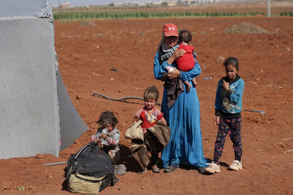 A woman with children stands by a tent area, on land between Deraa and Sweida, after scores of people have been killed this week in violence in and around the predominantly Druze city of Sweida, pitting fighters from the Druze minority against government security forces and members of Bedouin tribes, in Deraa, Syria July 17, 2025. REUTERS/Khalil Ashawi