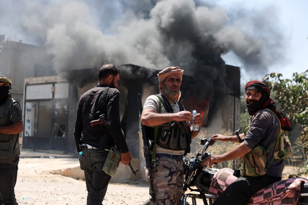 TOPSHOT - Heavy smoke rises from a burning building as fighters from Bedouin tribes gather in al-Mazraa village, in Syria's southern Sweida governorate on July 18, 2025. The southern province has been gripped by deadly sectarian bloodshed since July 13, with hundreds reportedly killed in clashes pitting Druze fighters against Sunni Bedouin tribes and the army and its allies. (Photo by OMAR HAJ KADOUR / AFP)

