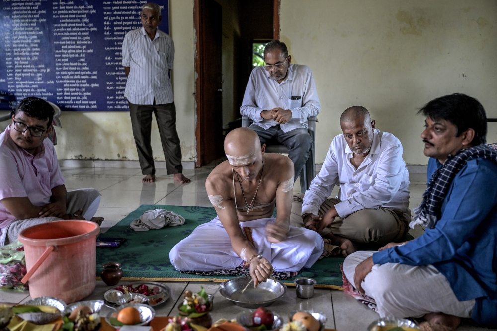 Anil Ambalal Patel (sitting on floor in while shirt, right) participates in rituals with Harshad Patel, his son-in-law, after immersing ashes in the Narmada river in Ahmedabad, India, June 24, 2025. (Atul Loke/The New York Times)