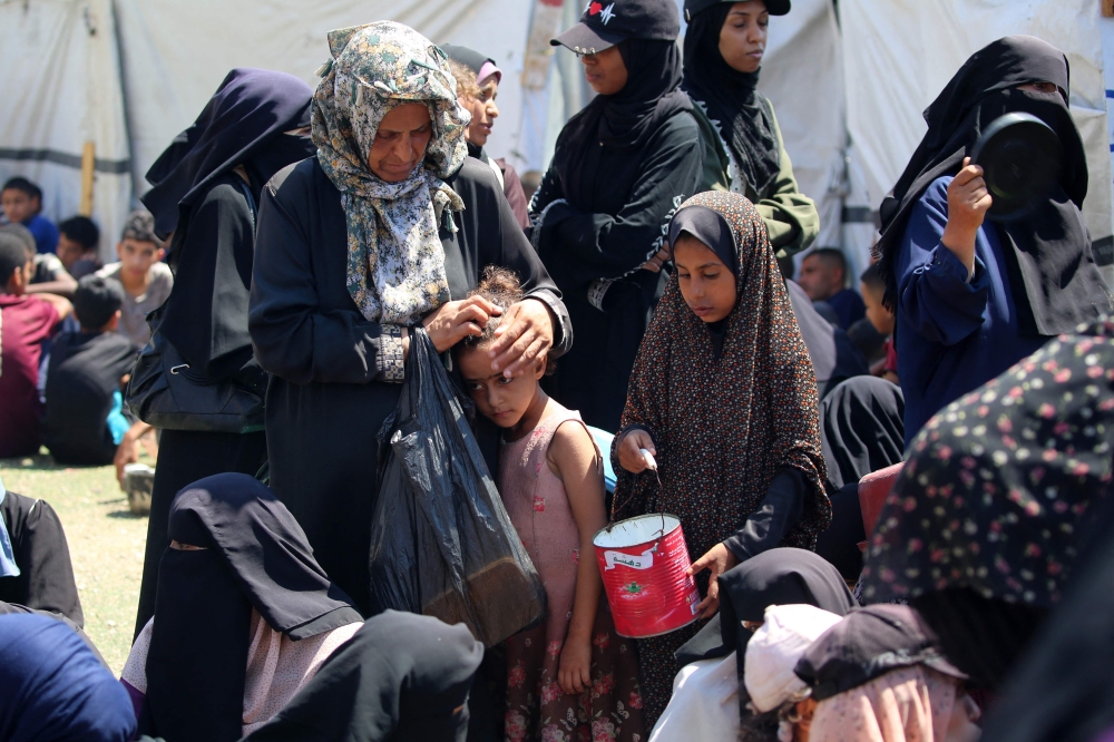 A woman caresses a child's head as Palestinians wait at a food distribution point in the Nuseirat refugee camp. — AFP
