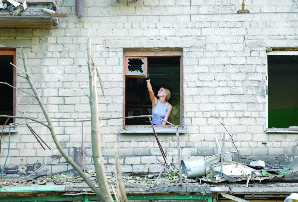 A woman removes a broken glass in a damaged apartment building, in Donetsk. — Reuters