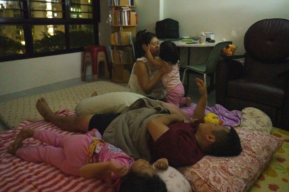 Ho Kin Ing and her husband, Tan Peng Yong, prepare their daughters for bed in their living room in Singapore, June 2, 2025.  (Ore Huiying/The New York Times)