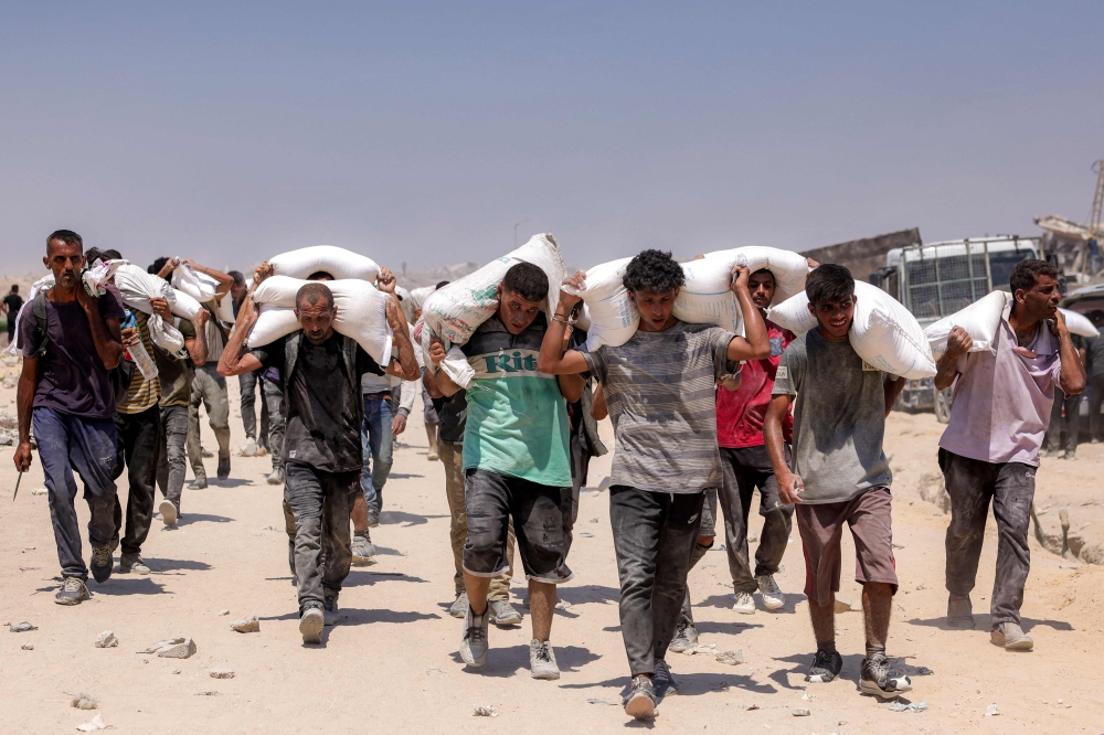 People walk with sacks of flour delivered after trucks carrying humanitarian aid entered northern Gaza on July 27, 2025 coming from the Zikim border crossing