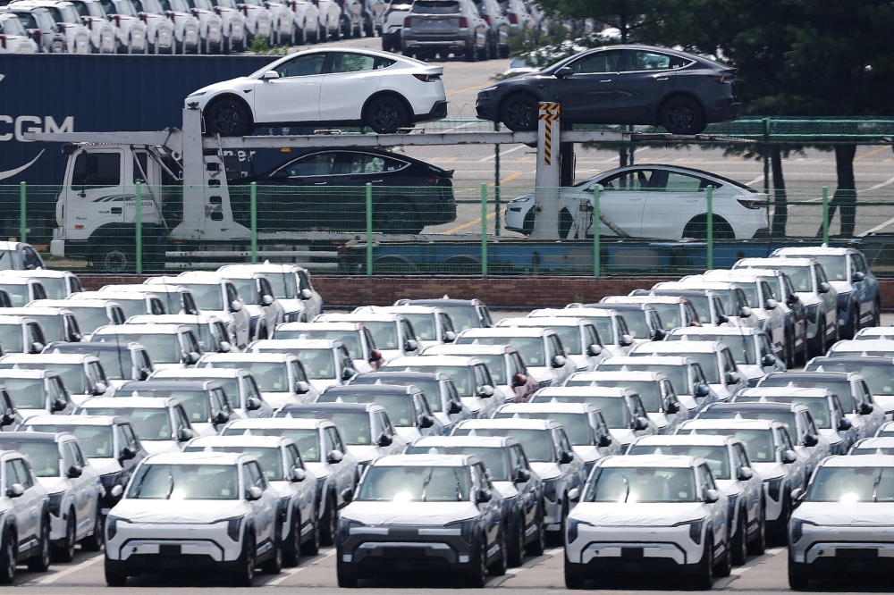 A car carrier transporting Tesla vehicles travels past KIA Motors' vehicles parked at a port in Pyeongtaek, South Korea, July 31, 2025.    
