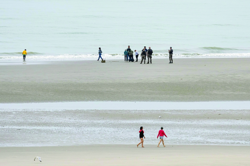 French gendarmes stand with migrants as they wait to board a smuggler's boat in an attempt to cross the English Channel off the beach of Equihen, northern France. - AFP
