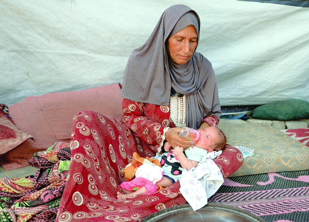 Nemah Hamouda holds her three-month-old granddaughter, Muntaha, in her arms while feeding her with a homemade herbal mixture, amid a severe shortage of infant formula and rising malnutrition, in Gaza City. - Reuters