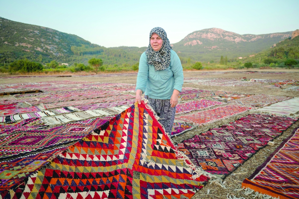 A worker holds an handwoven carpet laid out in an open field to soften its colours under sizzling sun in Dosemealti district in Antalya on July 22, 2025. Thousands of carpets and kilims spread out in the sun form a festive and colourful patchwork on the outskirts of Antalya, the large coastal tourist city in southern Turkey. From June to September, in the harvested fields cleared of stubble, traders bring their cargoes to age in the sun, tempering the overly bright hues of their natural colours under its rays and ridding them of any unwanted elements. (Photo by Ozan KOSE / AFP)
