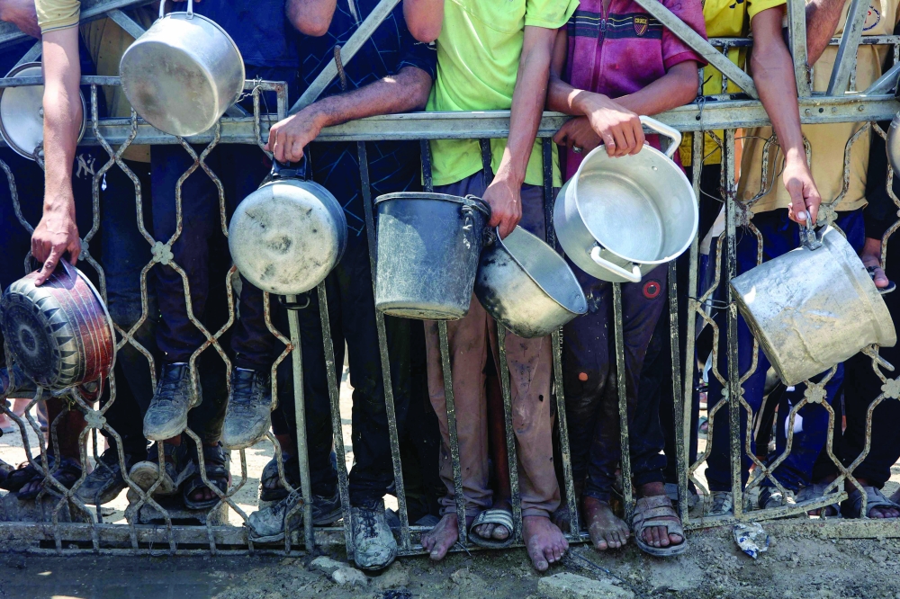 
Palestinians carry empty pots as they wait to receive lentil soup at a food distribution point in Gaza City on Saturday. — AFP 