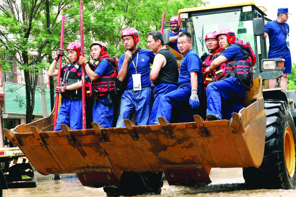 
Rescue workers ride on a front loader as they make their way through a flooded road, in Beijing. — Reuters file photo 