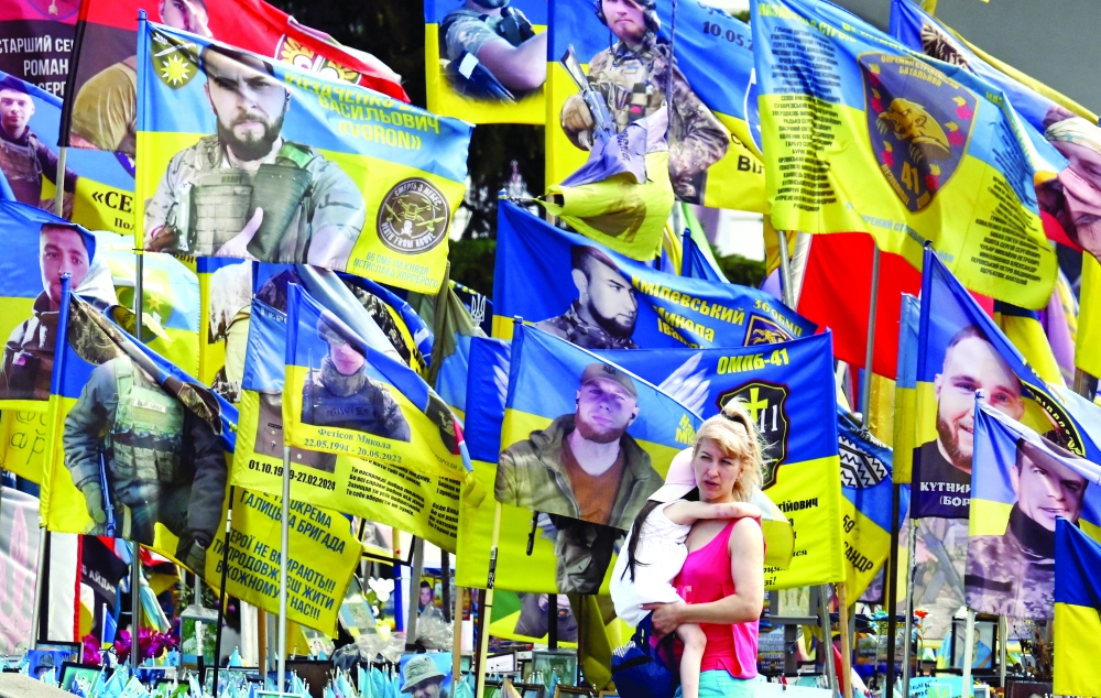 
A woman carrying a child walks at a memorial for fallen soldiers in Kyiv. — AFP 