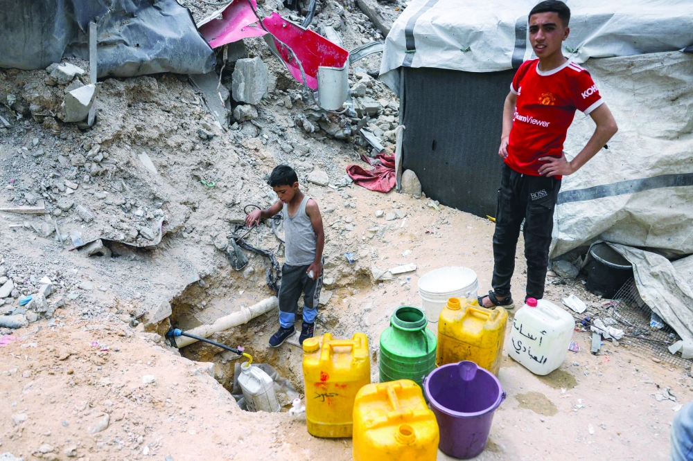 
A boy fills up containers with water from the remaining water still left in underground pipes, in Beit Lahia. — AFP 