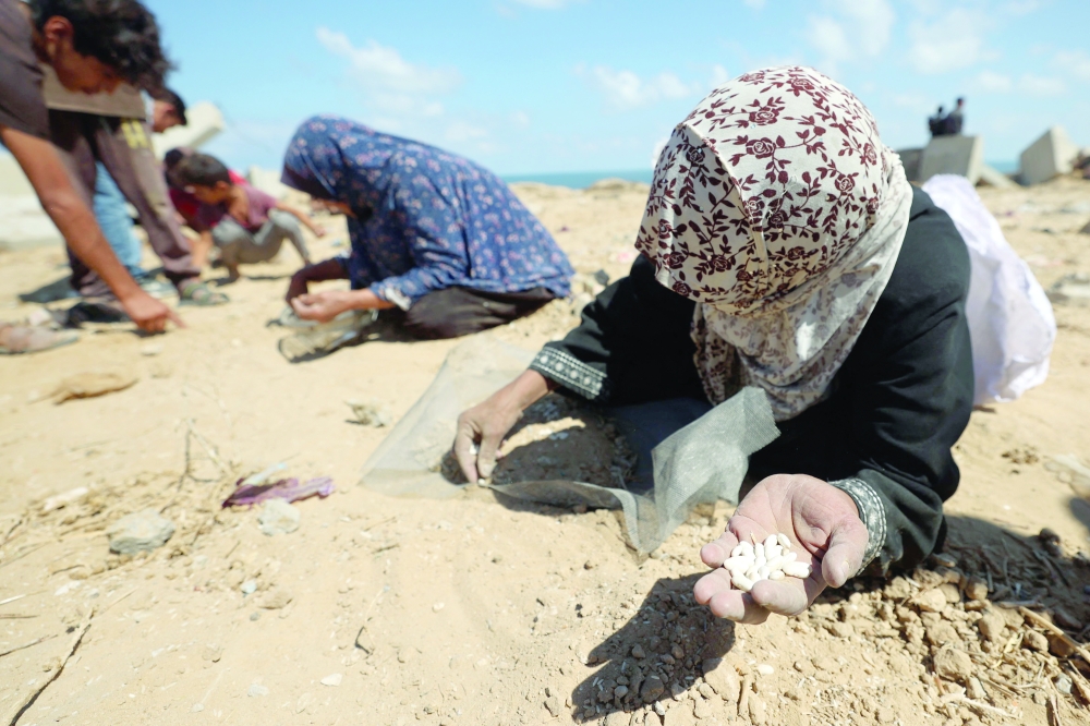 
Women search the sand for legumes or rice in Nuseirat on Tuesday. — AFP 