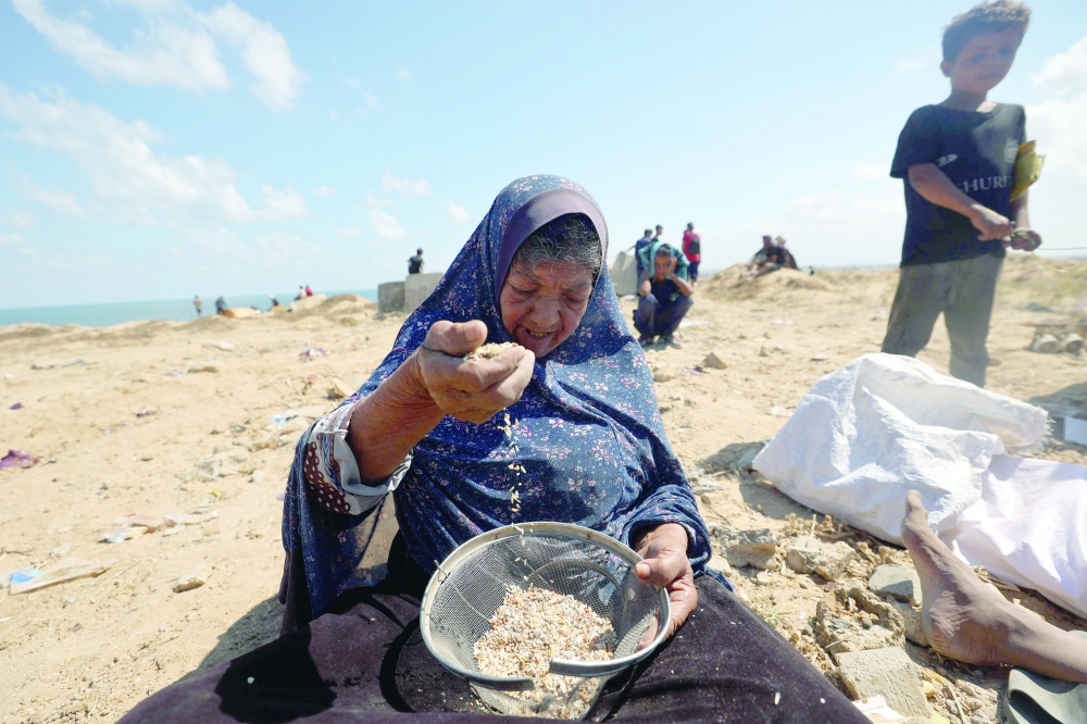 
A Palestinian woman uses a sieve on the sand as she searchces legumes or rice in Nuseirat in the central Gaza Strip during an airdrop mission above the Israel-besieged Palestinian territory on Tuesday. — AFP 