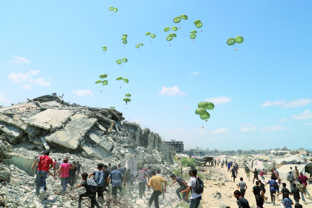 
Palestinians run towards parachutes carrying aid packages airdropped over northern Gaza Strip. — Reuters 