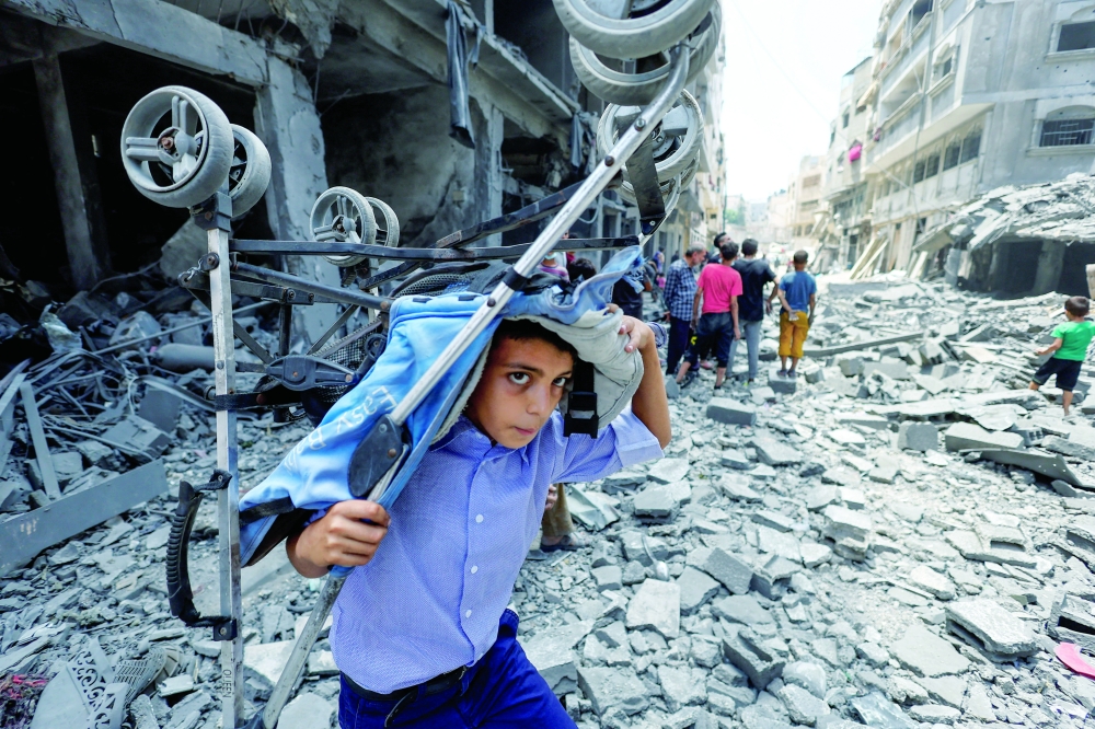 A Palestinian boy carries a stroller at the site of a morning Israeli strike on a house in Gaza City. — Reuters