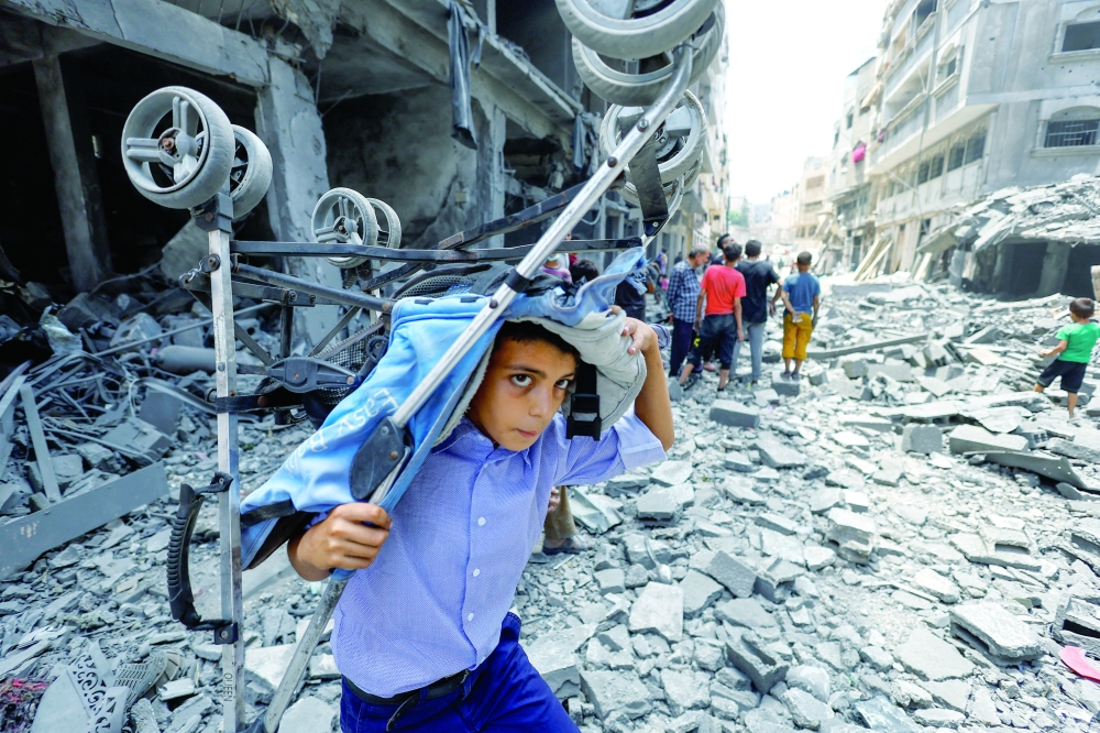 A boy carries a stroller at the site of an Israeli strike on a house in Gaza on Friday. — Reuters