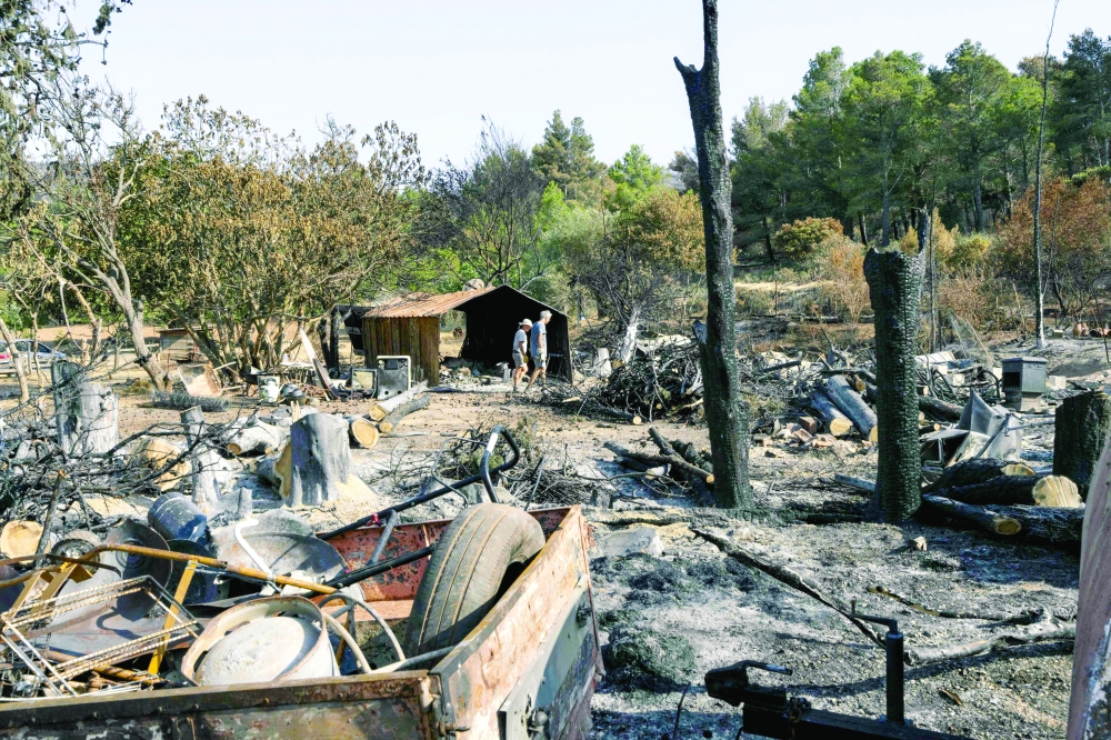 People walk through a burnt-out farm following wildfires in Fontjoncouse, France. — AFP