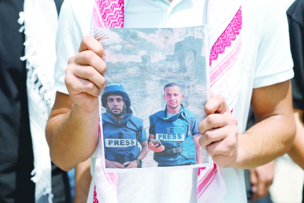 A Palestinian man holds up a print-out of a photograph as people protest against the killing of journalists in Gaza, at Birzeit University near Ramallah, on Monday. - Reuters